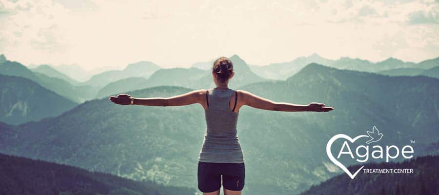woman stands on a mountainside with her arms open after quitting drinking