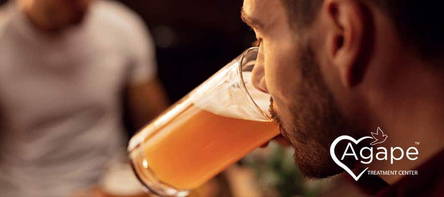 man with beard drinking a full glass of beer