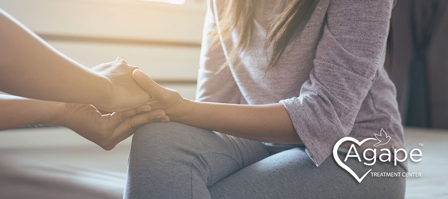 person holding hands with a woman struggling with alcoholism sitting on a couch